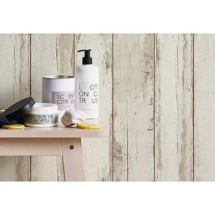 A.S. Création Il Decoro Vliestapete Vintage-Wood - Beige, Holzoptik, 10,05 x 0,53 m - Nahaufnahme von Körperpflegeprodukten wie Lotion, Peeling und Duftkerze mit Zitrusduft auf einem kleinen Tisch.