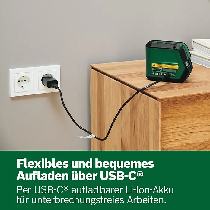 Bosch Kreuzlinienlaser Advanced Level 2G - Max. Arbeitsbereich: 15 m - Ein grünes und schwarzes Laser-Nivellier lädt über ein USB-C-Kabel an einer Steckdose auf einem Holzschrank auf.
