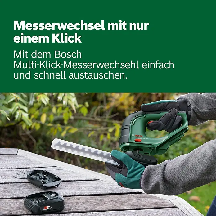 Bosch Power for All 18V Akku-Gras- & Strauchschere AdvancedShear 18V-10 - 18 V, Li-Ionen, 1 Akku, Schwertbreite: 10 cm - Grüne Bosch AdvancedShear 18V mit wechselbarem Messer. Eine Hand hält das Gerät, Zubehör liegt auf einem Holztisch.
