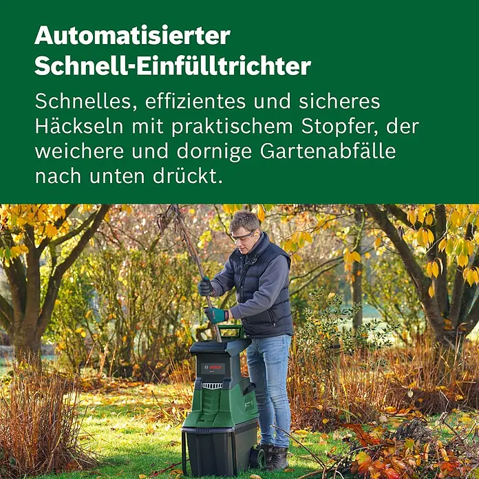 Bosch Elektro-Häcksler AXT 25 TC - Max. Aststärke: 4,5 cm, 2.500 W - Ein Mann im Garten nutzt einen grün-schwarzen Bosch Gartenhäcksler zum Zerkleinern von Ästen.
