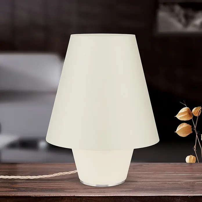 Orion Leuchten Tischleuchte - 40 W, L x B x H: 25 x 25 x 30 cm, E27 - Eine cremefarbene Tischleuchte mit konischem Stoffschirm und leuchtendem Sockel steht auf einem Holztisch. Ein geflochtenes Netzkabel ist sichtbar.