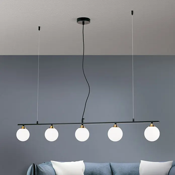 Orion Leuchten Pendelleuchte - L x B x H: 120 x 12 x 150 cm, G9 - Schwarze lineare Pendelleuchte mit fünf weißen Glaskugelschirmen und Messingakzenten, über einem Sofa hängend.