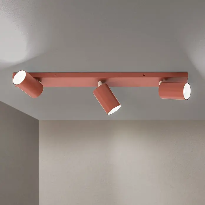 Orion Leuchten Deckenstrahler - L x B x H: 60 x 6 x 2 cm, GU10 - Lachsfarbener Deckenstrahler mit drei verstellbaren zylindrischen Leuchten an einer rechteckigen Stange, beleuchtet eine Raumecke.