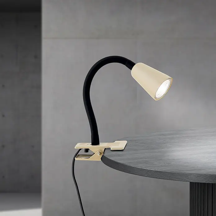 Orion Leuchten Klemmleuchte - 40 W, L x B x H: 7,5 x 16,5 x 27 cm - Creme Clip-Klemmleuchte mit schwarzem Flexarm, beleuchtet einen dunkelgrauen Tisch.
