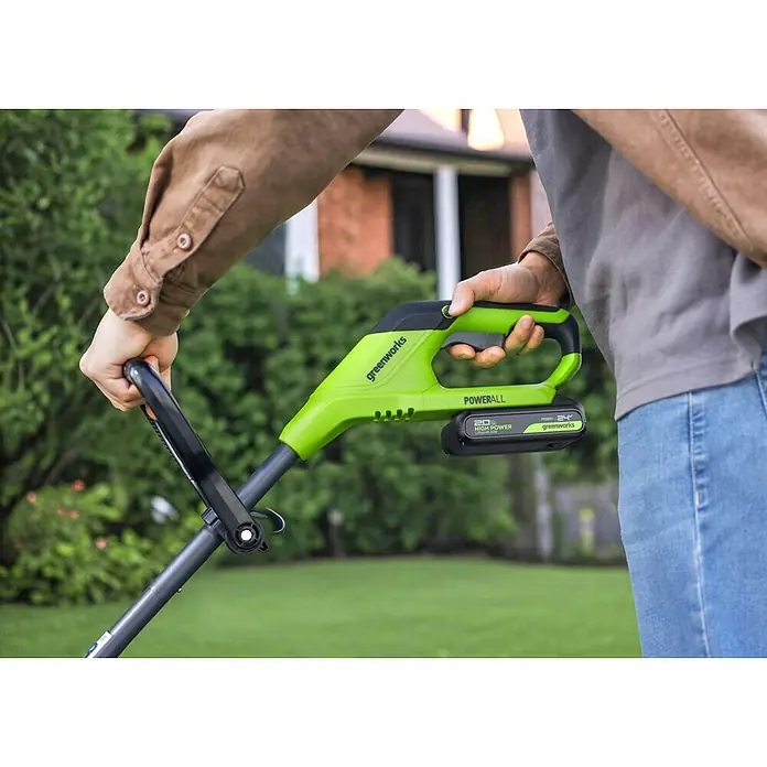 Greenworks Akku-Rasenmäher-Set - 24 V, 1 Akku, Schnittbreite: 33 cm - Person hält ein grün-schwarzes Greenworks Elektro-Gartengerät mit 24V Lithium-Ionen-Akku.