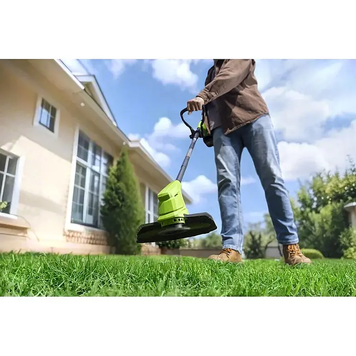 Greenworks Akku-Rasenmäher-Set - 24 V, 1 Akku, Schnittbreite: 33 cm - Eine Person trimmt Gras mit einem grün-schwarzen Rasentrimmer in einem Garten vor einem Haus.