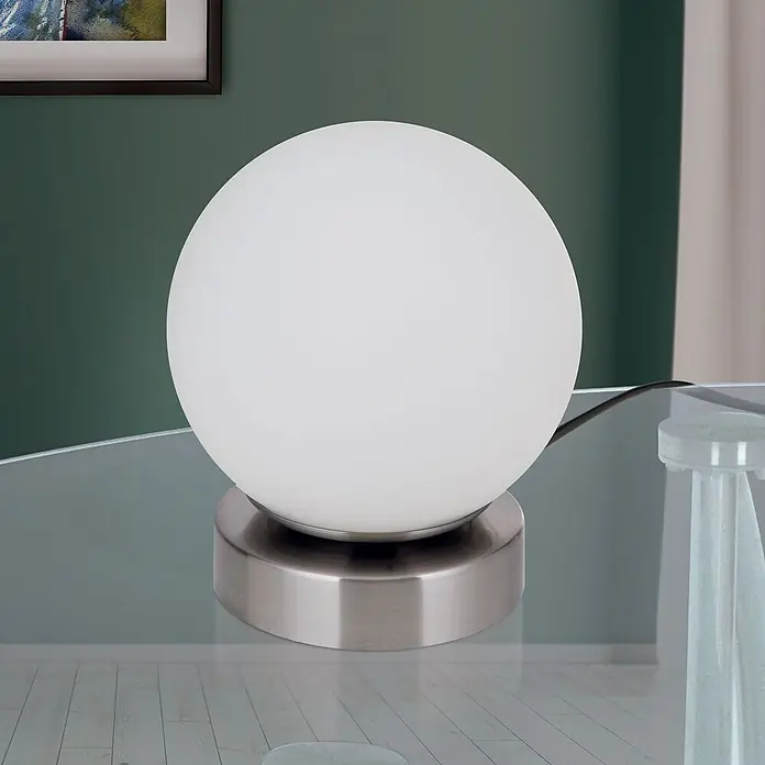 Orion Leuchten LED-Tischleuchte - 3 W, L x B x H: 12,6 x 12,6 x 14 cm, Warmweiß - Weiße kugelförmige Glastischlampe mit gebürstetem Stahlfuß, auf einem Glastisch in einem Raum.