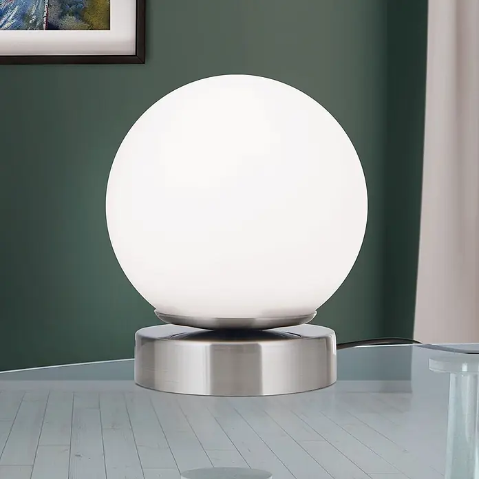 Orion Leuchten LED-Tischleuchte - 3 W, L x B x H: 12,6 x 12,6 x 14 cm, Warmweiß - Sphärische Tischlampe mit weißem Glasdiffusor und gebürstetem Metallsockel auf einem Glastisch.