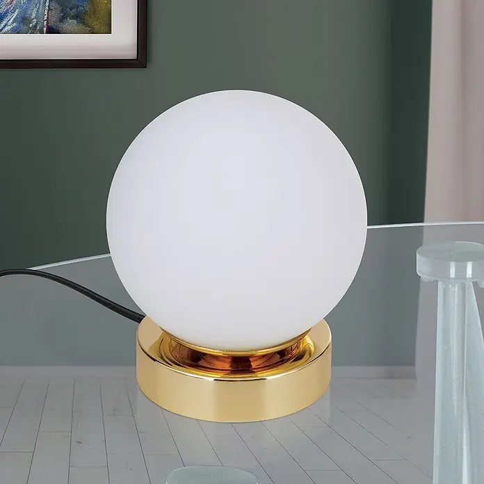 Orion Leuchten LED-Tischleuchte - 3 W, L x B x H: 12,6 x 12,6 x 14 cm, Warmweiß - Eine kugelförmige weiße Tischlampe mit glänzendem goldenem Sockel auf einem Glastisch.