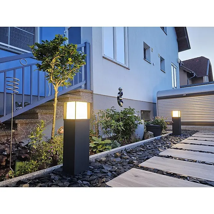 Orion Leuchten Außensockelleuchte - 16 x 16 x 60 cm, Ohne Leuchtmittel - Dunkle quadratische Pollerleuchte erhellt einen Gartenweg mit warmweißem Licht, platziert zwischen Steinen und Pflanzen.