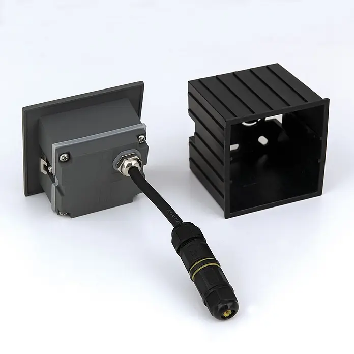 Orion Leuchten LED-Einbauleuchte -  - Grauer Elektro-Anschlusskasten mit angeschlossenem schwarzem Kabel und abgedichtetem Stecker, neben einem schwarzen gerippten Gehäuse.