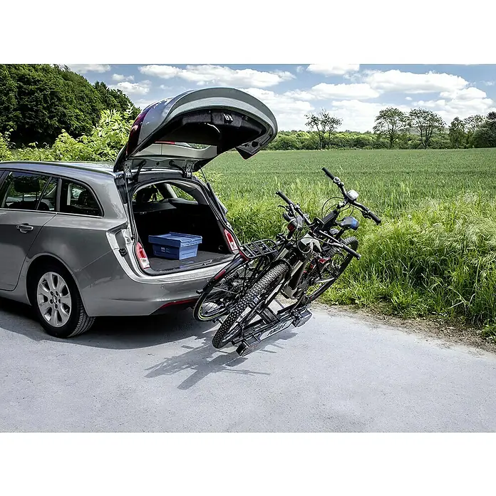 Eufab Fahrradträger Poker-F - Geeignet für: 2 Fahrräder, Traglast: 60 kg, Passend für: Fahrzeuge mit Anhängerkupplung - Silberner Opel Insignia mit geöffneter Heckklappe und montiertem Fahrradträger mit zwei Fahrrädern auf einer Landstraße.