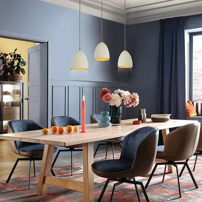 Just Light Pendelleuchte Traventa - L x B x H: 115 x 21 x 120 cm, Travertinoptik, E27, Anzahl Leuchtmittel: 3 Stk. - Drei cremefarbene Pendelleuchten mit goldener Innenseite hängen über einem Holztisch.