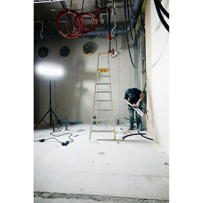 Mareld LED-Strahler Vapor 20000 App & Sensor - 200 W, 20.000 lm, 6.500 K, L x B x H: 43 x 6,7 x 32 cm, IP65 - Arbeiter installiert Kabel in einem Rohbau mit Leiter und heller Beleuchtung.