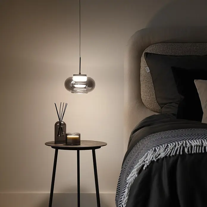 Just Light LED-Pendelleuchte Sia - 4,5 W, L x B x H: 80 x 20 x 20 cm, Rauchglas/ Schwarz, Warmweiß, Anzahl Leuchtmittel: 1 Stk. - Pendelleuchte aus Rauchglas beleuchtet einen Nachttisch mit Diffusor und Kerze in einer gemütlichen Schlafzimmerecke.