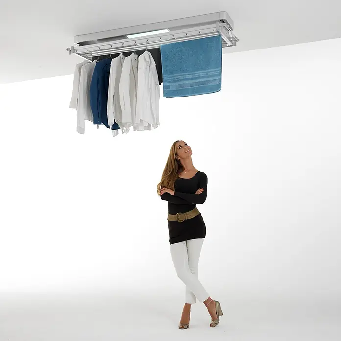 Foxydry Deckenwäschetrockner Pro 120 - L x B: 53 x 122 cm, Stahlgrau - Deckenmontierter Wäschetrockner in Silber mit integriertem Licht, hält Kleidung und ein blaues Handtuch, von einer Frau betrachtet.