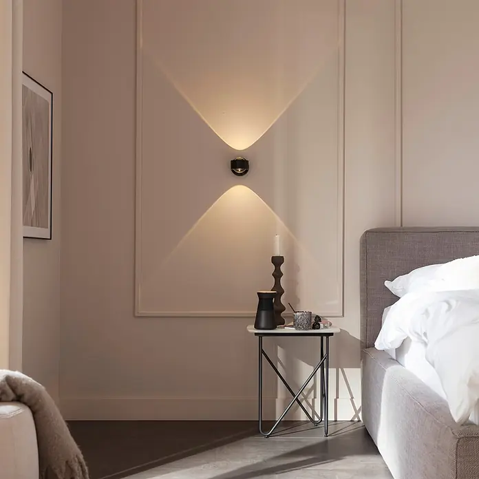 Just Light LED-Wandleuchte Chia -  - Runde schwarze Wandleuchte an einer Wand, die Lichtmuster nach oben und unten in einem Schlafzimmer wirft.