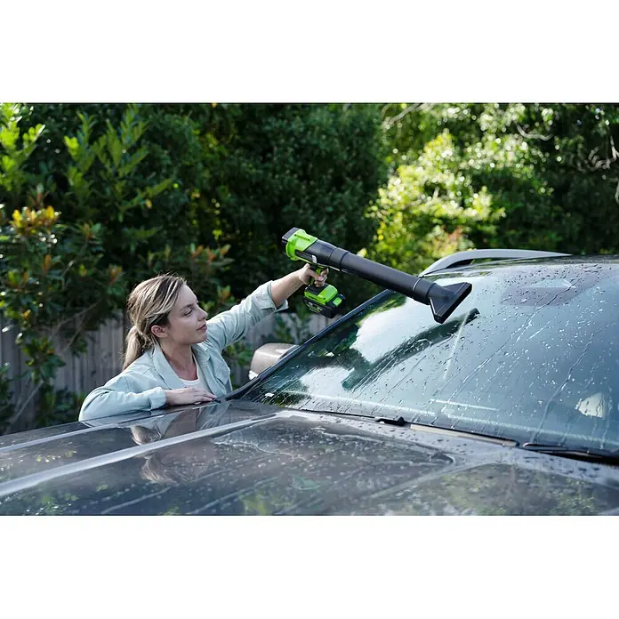 Greenworks Akku-Laubbläser GW 24V BL - 24 V, 1 Akku, 2 Ah, Blasgeschwindigkeit: 209 km/h, Blasleistung: 7,6 m³/h - Frau trocknet mit grün-schwarzem Handgebläse eine Autoscheibe.