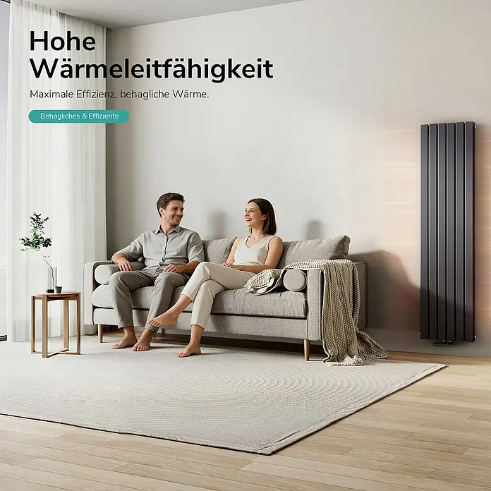 Emke Designheizkörper Flatrad FR - Wärmeleistung bei Vorlauftemperatur von 75 °C (D: 50): 1.670 W, Anthrazit - Hoher, dunkelgrauer Plattenheizkörper wärmt ein modernes Wohnzimmer, in dem sich ein Paar auf einem Sofa entspannt.