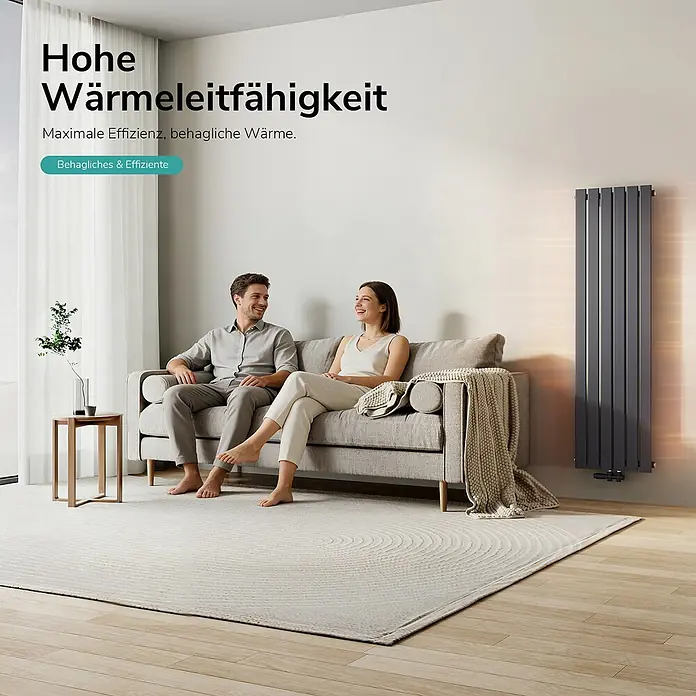 Emke Designheizkörper Flatrad FR - Wärmeleistung bei Vorlauftemperatur von 75 °C (D: 50): 850 W, Anthrazit - Hoher, anthrazitgrauer Vertikalheizkörper wärmt ein gemütliches Wohnzimmer, in dem ein Paar auf einem Sofa entspannt.