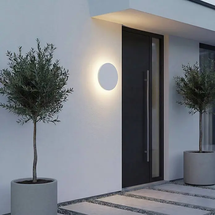 Lindby Außenwandleuchte Selinel - weiß / opal, weiß / opal, IP65 - Moderne, runde, weiße Außenwandleuchte beleuchtet einen Eingang neben einer dunklen Tür.