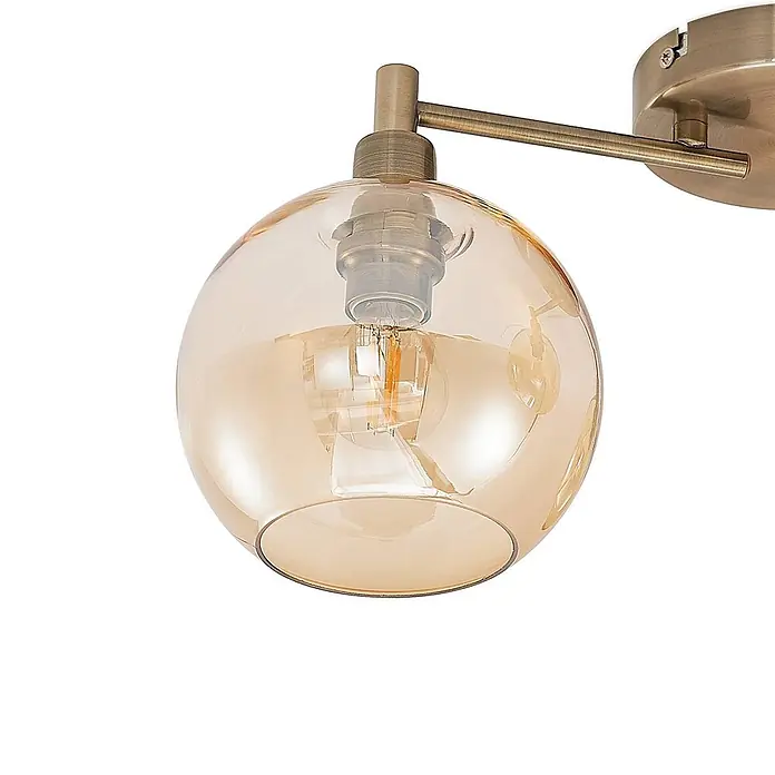 Lindby Deckenleuchte Jemissa - messing / gold, creme / amber, E14 - Lampe mit bernsteinfarbener Glaskugel und messingfarbenem Metallarm, zeigt eine Glühbirne.