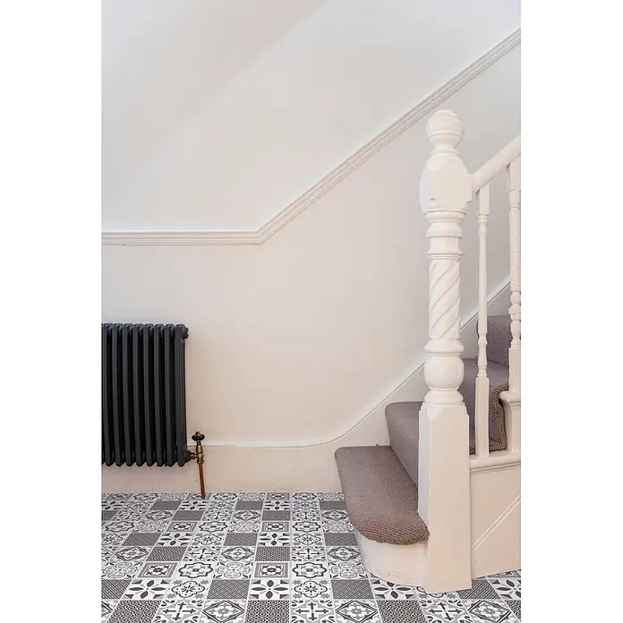 D-c-fix Bodenfliese Floor Tile Selbstklebend - 11 Stk., 30,5 x 30,5 cm, Oriental Tiles - Grau-weiße gemusterte Bodenfliesen in einem Flur neben einem dunklen Heizkörper und einer Teppichtreppe.