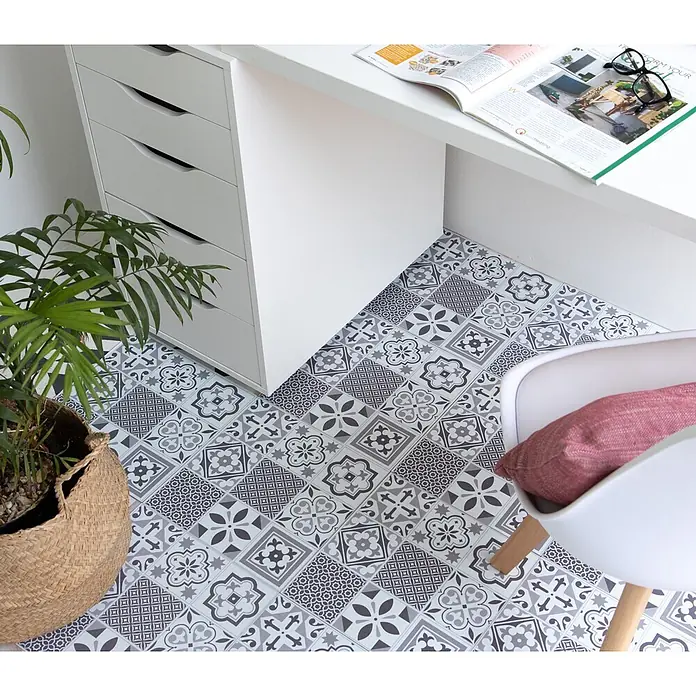 D-c-fix Bodenfliese Floor Tile Selbstklebend - 11 Stk., 30,5 x 30,5 cm, Oriental Tiles - Grau-weiße gemusterte Bodenfliesen im Patchwork-Design bilden eine stilvolle Oberfläche unter einem Schreibtisch und Stuhl.