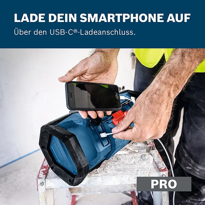 Bosch Professional AMPShare 18V Akku-Radio GPB 18V- 3 C SOLO K - 18 V, Ohne Akku - Eine Person lädt ein Smartphone über ein USB-C-Kabel an einer blau-schwarzen Arbeitsleuchte.