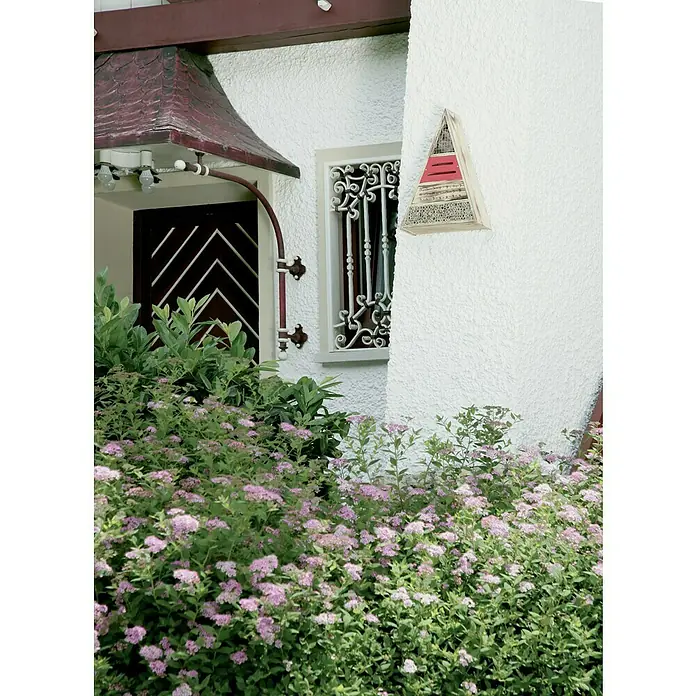 Windhager Insektenhotel - L x B x H: 36,5 x 9,5 x 48,5 cm, Holz, Naturbraun/Rot, Geflammt - Die Aufnahme zeigt ein Haus mit einer Tür, einem Fenster mit Ziergitter und einem dreieckigen Wandschmuck, umgeben von blühenden Büschen.