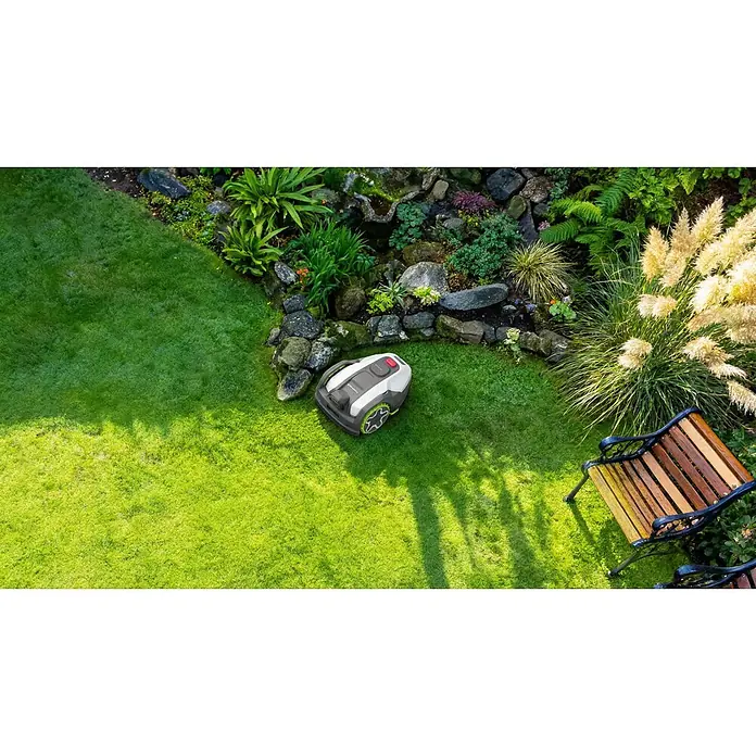 Greenworks Mähroboter AI Mowbot 10 GW KI RTK+VISION - 1.000 m², Schnittbreite: 20 cm, Satellitengestützte Navigation, RTK - Grauer und weißer Rasenroboter mit grünen Rädern parkt auf einem Rasen im Garten.