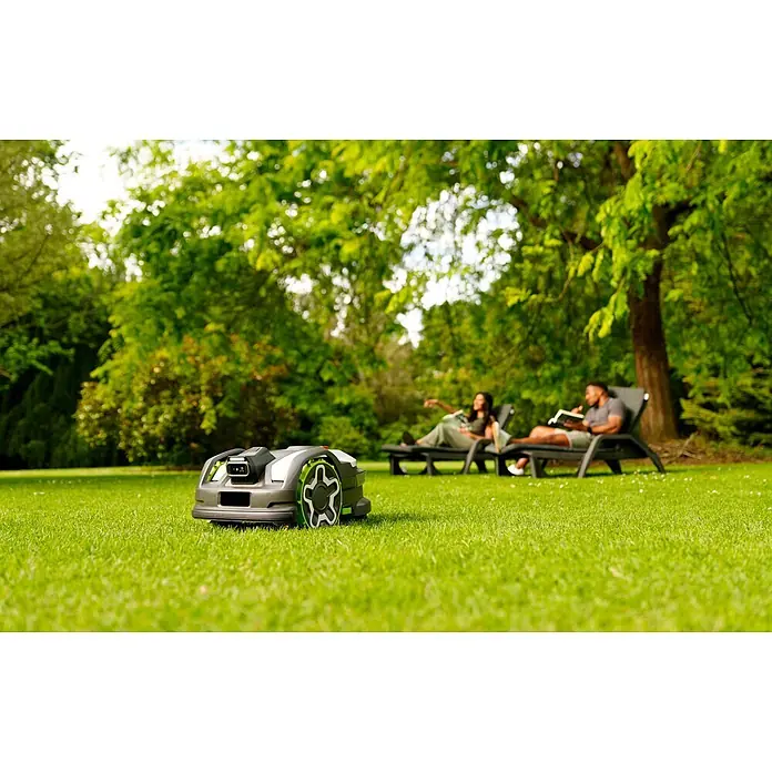 Greenworks Mähroboter AI Mowbot 10 GW KI RTK+VISION - 1.000 m², Schnittbreite: 20 cm, Satellitengestützte Navigation, RTK - Grau-weißer Rasenroboter mit grünen Akzenten auf einem Rasen, während zwei Personen im Hintergrund entspannen.