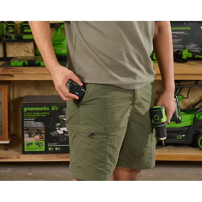 Greenworks Akku & Ladegerät 24V 4 AH, VD - Akkuspannung: 24 V, Li-Ionen, 4 Ah - Person hält ein schwarzes Greenworks 65W Netzteil und einen grünen Greenworks Akkuschrauber.