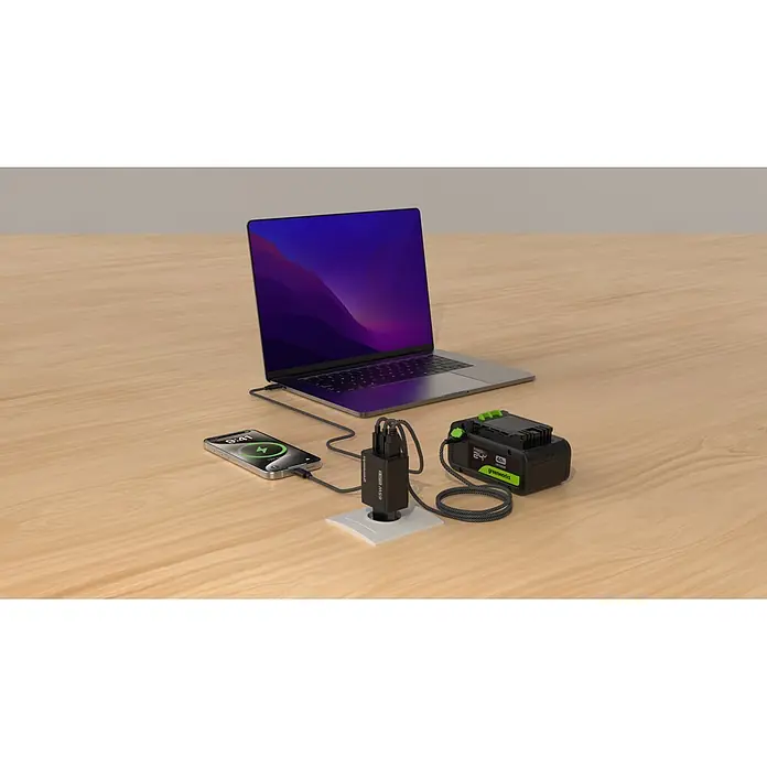 Greenworks Akku & Ladegerät 24V 2 AH, VD - Akkuspannung: 24 V, Li-Ionen, 2 Ah - Ein Greenworks 65W GaN II Multi-Port-Ladegerät lädt Laptop, Smartphone und Greenworks Akku gleichzeitig auf einem Holztisch.