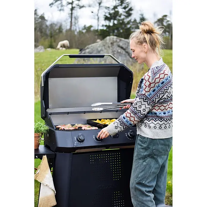 Cozze Grillzange - Länge: 40 cm - Frau grillt Fleisch und Kartoffeln auf einem schwarzen Cozze Gasgrill im Freien.