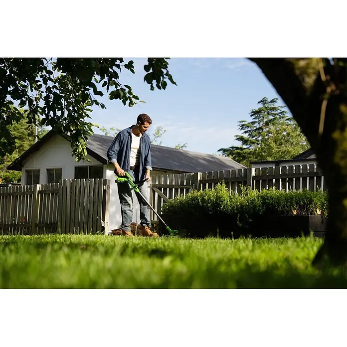 Greenworks Akku-Rasentrimmer 24V BL 30 cm - 24 V, 2 Ah, Li-Ionen, 1 Akku, Schnittbreite Messer: 30 cm, Schnittbreite Faden: 30 cm - Mann trimmt Gras mit einem grün-schwarzen Rasentrimmer im Garten.