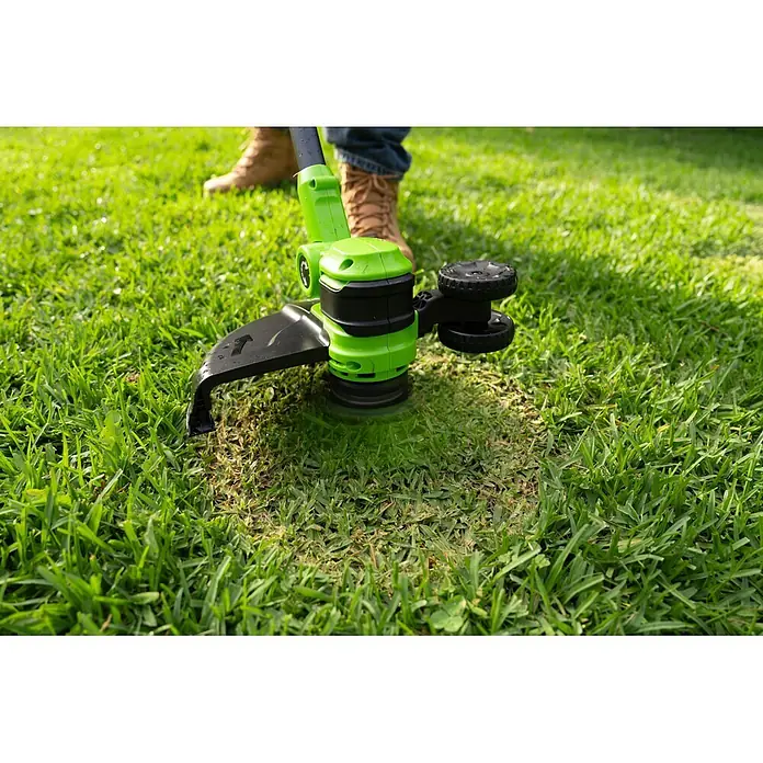 Greenworks Akku-Rasentrimmer 24V BL 30 cm - 24 V, 2 Ah, Li-Ionen, 1 Akku, Schnittbreite Messer: 30 cm, Schnittbreite Faden: 30 cm - Grün-schwarzer Rasentrimmer schneidet Gras, bedient von einer Person mit sichtbaren Stiefeln.
