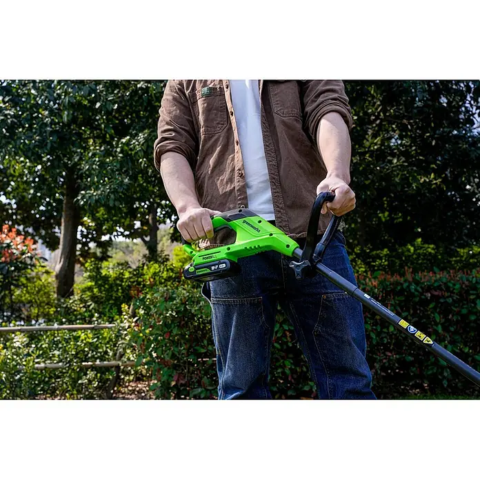 Greenworks Akku-Rasentrimmer 24V BL 25 cm - 24 V, Li-Ionen, Ohne Akku, Schnittbreite Messer: 25 cm - Eine Person hält einen grünen und schwarzen Greenworks Akku-Rasentrimmer mit 24V Akku.