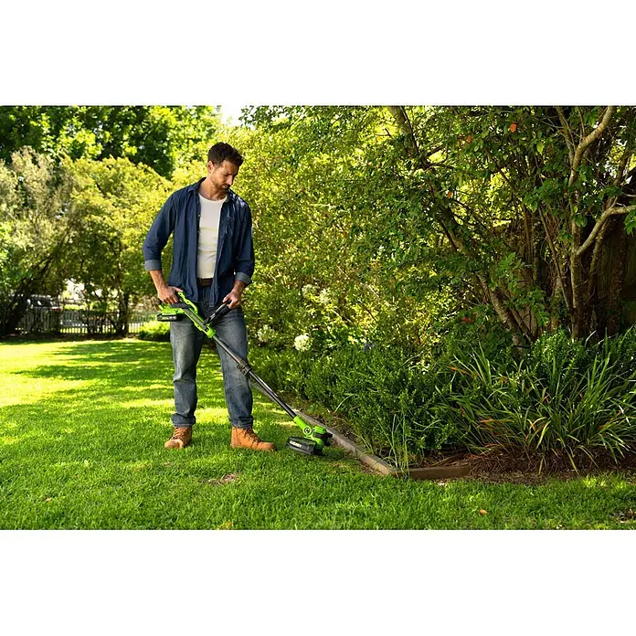 Greenworks Akku-Rasentrimmer 24V BL 30 cm - 24 V, 2 Ah, Li-Ionen, 1 Akku, Schnittbreite Messer: 30 cm, Schnittbreite Faden: 30 cm - Mann nutzt einen grün-schwarzen Rasentrimmer zum Kantenschneiden am Beet in einem sonnigen Garten.
