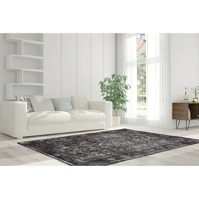 Kayoom Kurzflorteppich Vintage - Anthrazit, 200 x 140 cm, 100 % Polyacryl - Ein rechteckiger, dunkler Teppich mit orientalischem Muster liegt in einem hellen Wohnzimmer mit weißen Möbeln und viel Tageslicht.