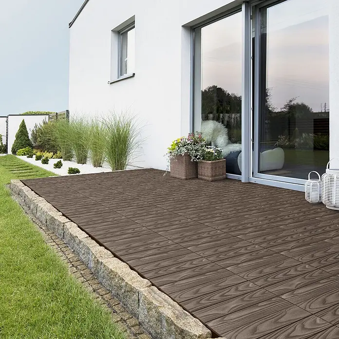 ML-Design Terrassenfliese Bodenbelag 4m²/44 Stück Dunkelbraun rutschfest Balkonfliesen - 30 cm x 30 cm x 20 mm, Dunkelbraun - Dunkelbraune WPC-Terrassenfliesen mit Holzmaserung bilden eine Terrasse neben einem Haus, umrandet von Stein.