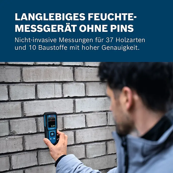 Bosch Feuchtigkeitsmessgerät GMM 1-15 - Messgenauigkeit: ± 0,4 mm/m, Mit Batterien - Person hält ein blaues Bosch Feuchtigkeitsmessgerät an eine Ziegelwand, zeigt 1,0 % Feuchtigkeit an. Berührungsloses Messgerät für Baustoffe.