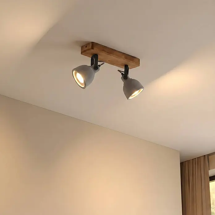 Lindby Deckenstrahler Mitis - Holz dunkel, alu / grau / zink, GU10 - Zwei verstellbare graue Strahler auf hellem Holzsockel an der Decke, die warmes Licht werfen.