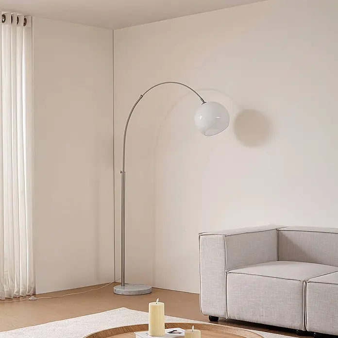 Lindby Stehleuchte Alverton - Höhe: 197 cm, alu / grau / zink, weiß / opal, E27 - Moderne Bogenstehlampe mit Silberfinish, Marmorfuß und weißem Kugelschirm, die eine Wohnzimmerecke beleuchtet.