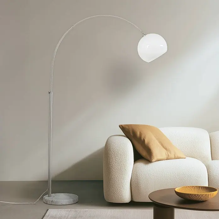 Lindby Stehleuchte Alverton - Höhe: 197 cm, alu / grau / zink, weiß / opal, E27 - Große Bogenstehleuchte mit Chromarm, weißer Glaskugel und Marmorfuß, neben einem weichen Sofa platziert.