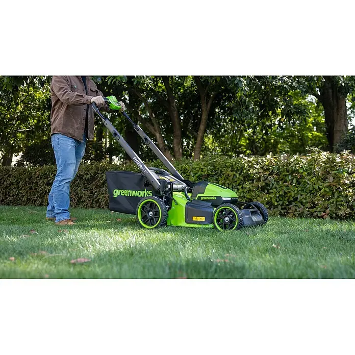 Greenworks Akku-Rasenmäher GW 2X24V BL 46 cm - 24 V, Ohne Akku, Schnittbreite: 46 cm - Ein Mann bedient einen grünen und schwarzen Greenworks Rasenmäher auf einem sonnigen Rasen.