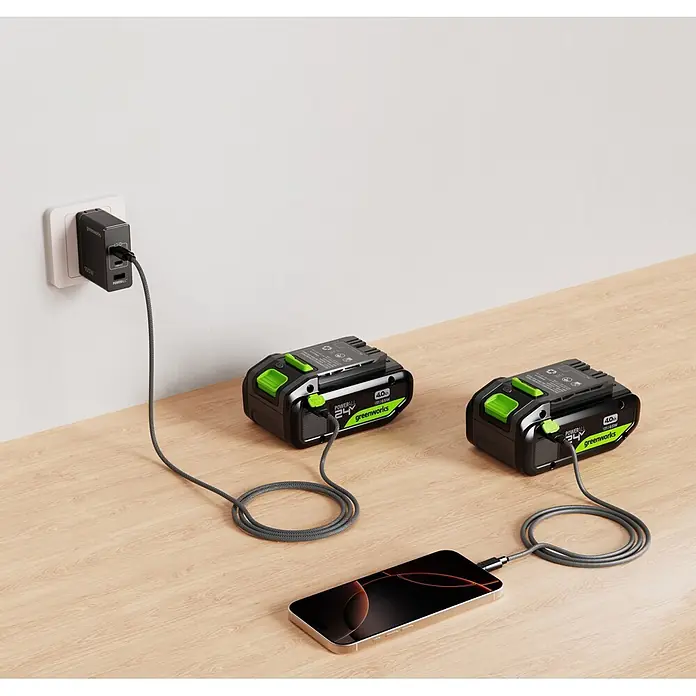 Greenworks Akku 24V 4 AH HP mit USB-C - 24 V, 4 Ah, Li-Ionen - Zwei schwarze und grüne Greenworks 4.0Ah Akkus laden, einer an einem Ladegerät, einer ein Smartphone.