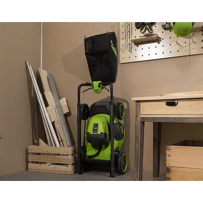 Greenworks Akku-Rasenmäher GW 2X24V BL 46 cm - 24 V, Ohne Akku, Schnittbreite: 46 cm - Leuchtend grüner Akku-Rasenmäher, platzsparend senkrecht in einer Werkstatt gelagert.