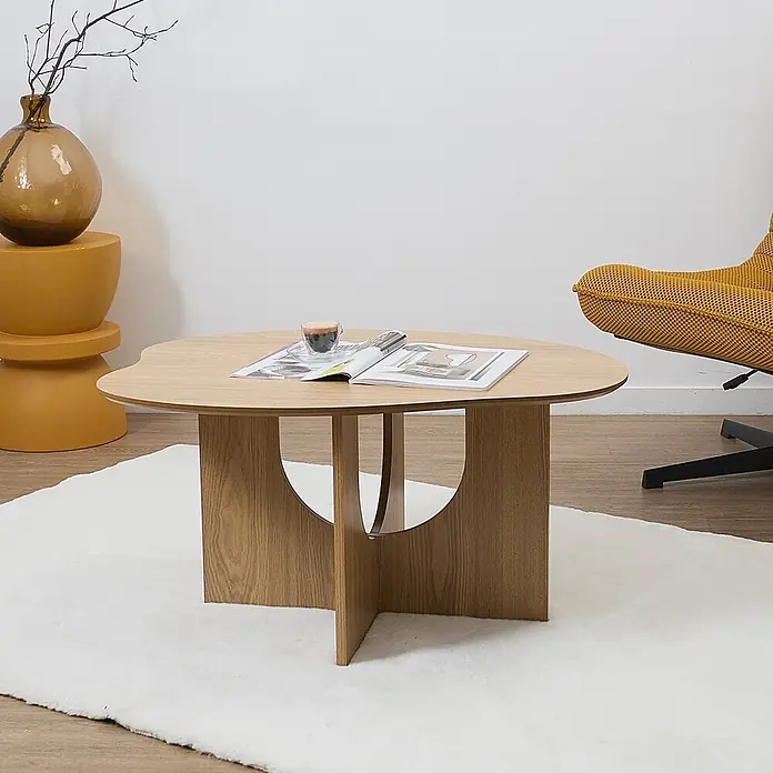 Home Deco Factory Calypso Mesa auxiliar - L x An x Al: 60 x 80 x 42 cm, MDF, Relieves curvos - Mesa de centro de madera clara con tablero redondeado y base de paneles cruzados con recortes circulares, mostrada en una sala de estar.