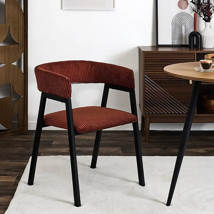 Home Deco Factory Silla Scott - Terracota, 2 ud. - Silla de comedor de pana naranja quemado con estructura y patas de metal negro, sobre una alfombra blanca junto a una mesa y un aparador de madera.